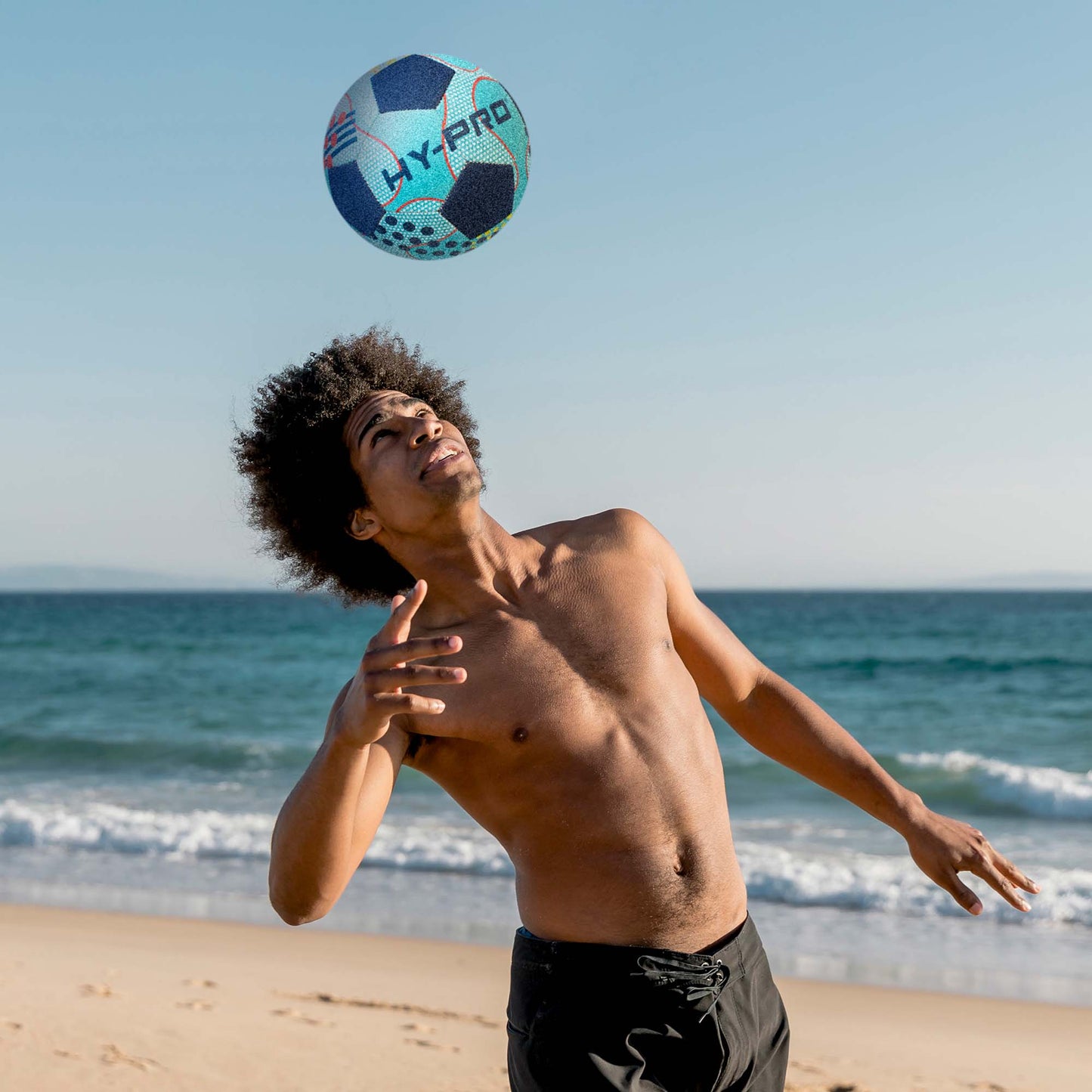 Hy-Pro size 5 Neoprene Football in blue with abstract design being used for tricks on a sandy beach