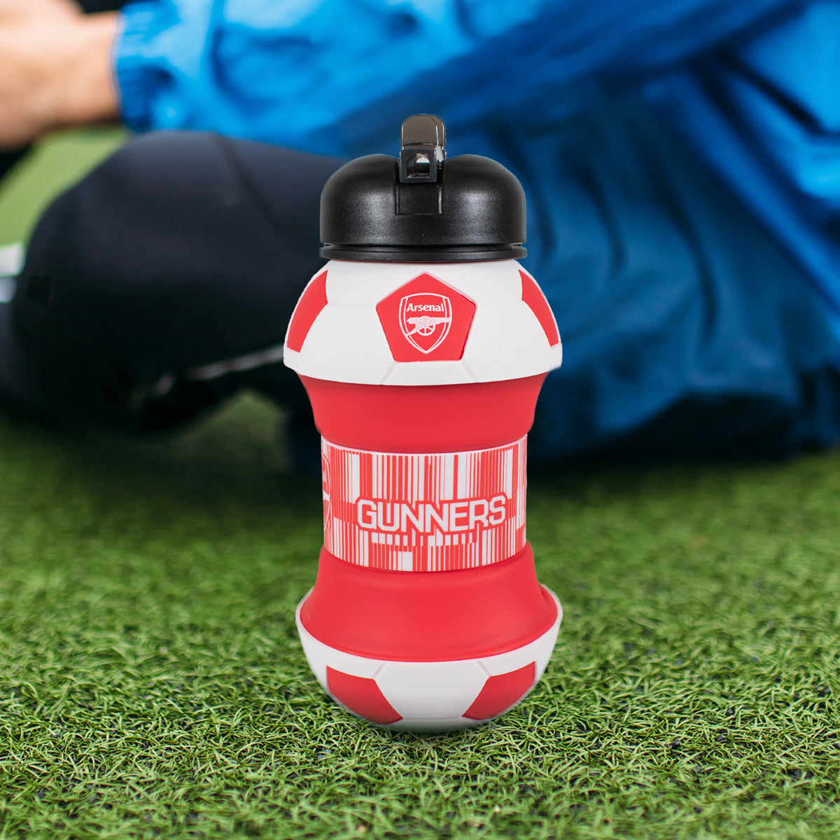 Arsenal gunners water bottle in red and white sat on a grass pitch next to a player