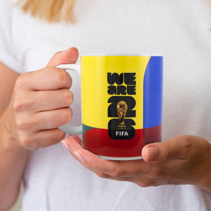 FIFA WORLD CUP 2026 CERAMIC MUG WITH WE ARE 26 BRANDING BEING HELD WITH A WHITE T-SHIRT IN THE BACKGROUND