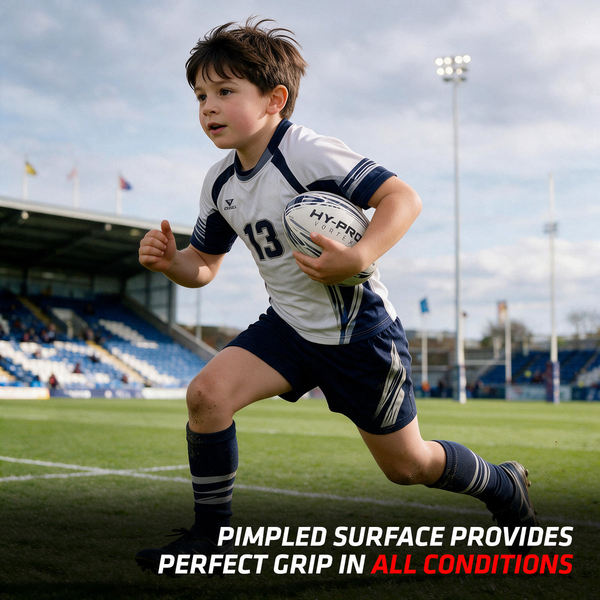 Small child runs along a rugby pitch holding the Hy-Pro Vortex Rugby Match Ball under his arm. The blue and white ball matches his blue and white kit