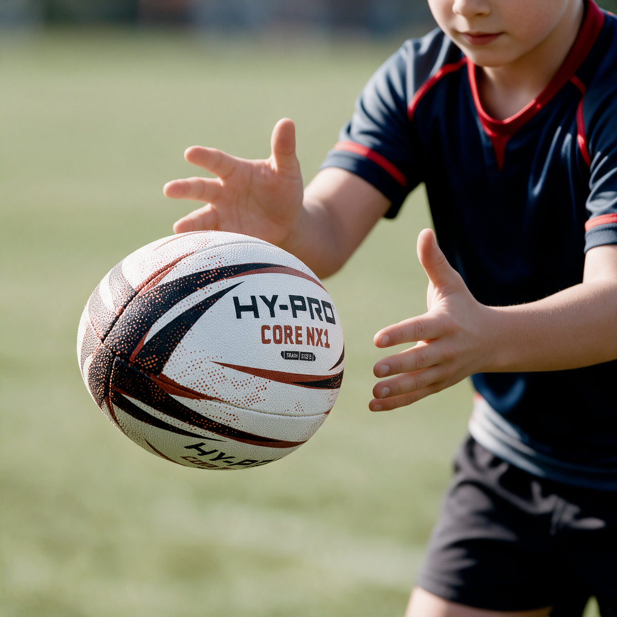 Hy-Pro Core NX1 Rugby Training Ball being passed by a young boy on a grass field.