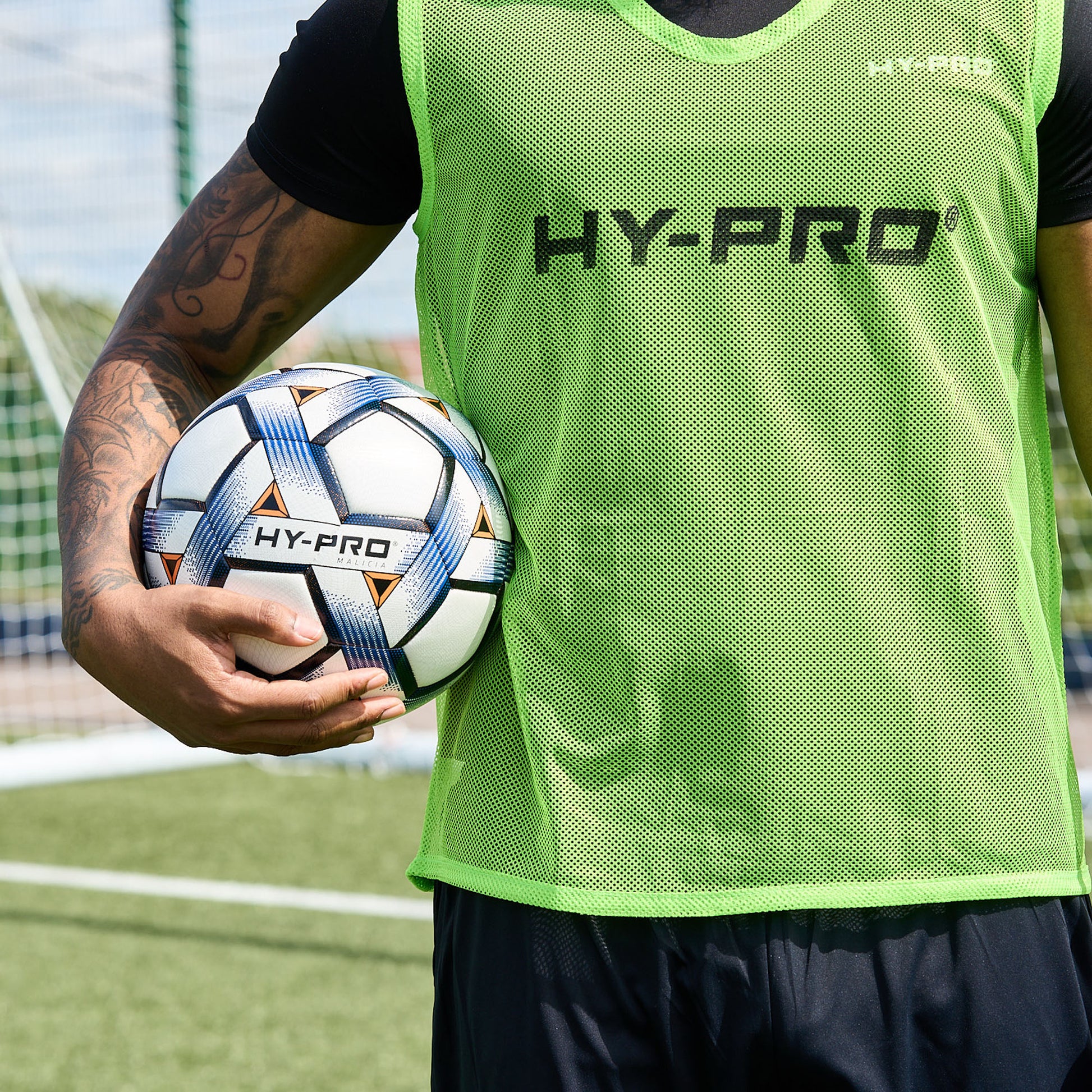 Hy-Pro Sports official FIFA certified training ball in blue and black being held by a football player wearing a bright green bib