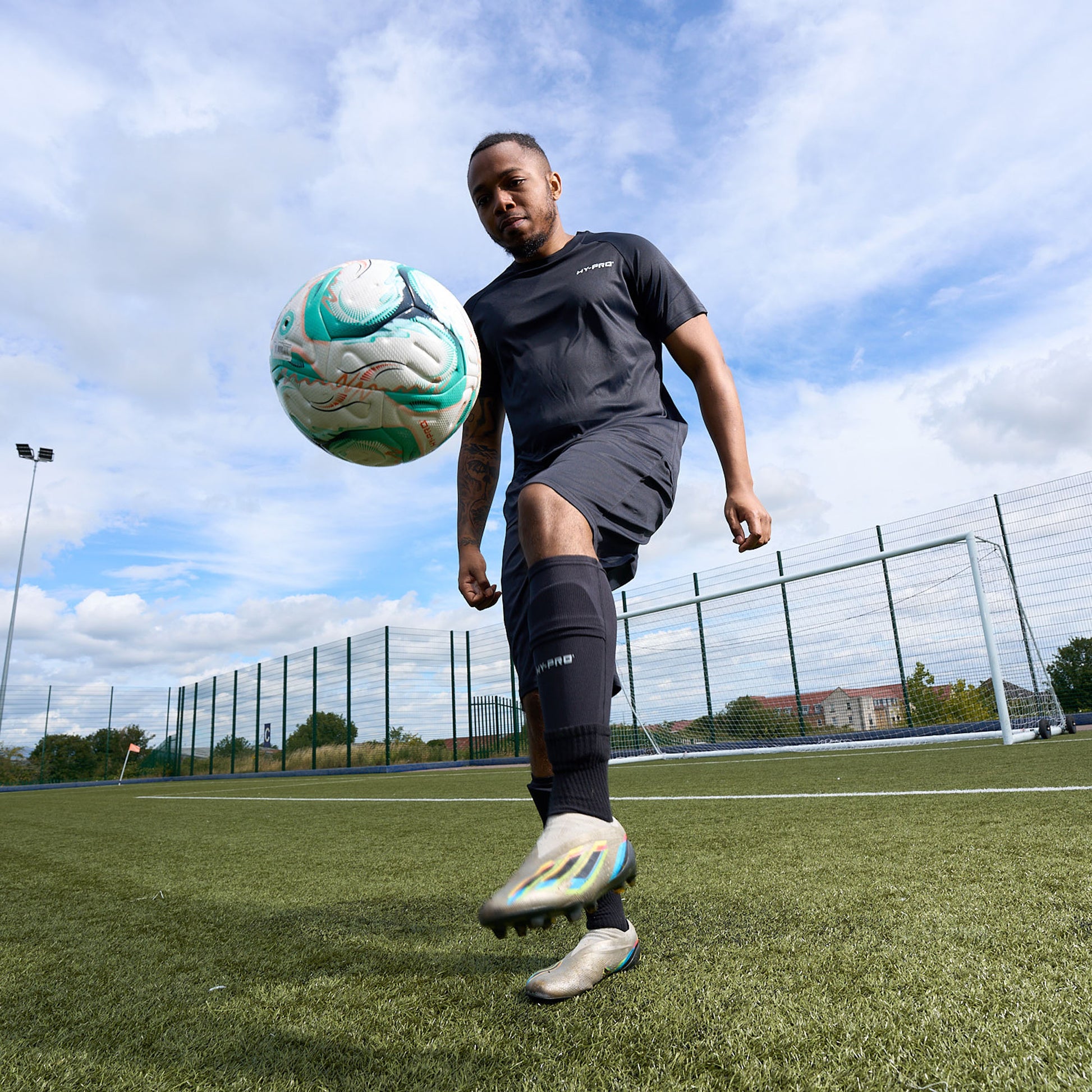 Hy-Pro Sports Shin Pads being worn by a football player kicking a football into the air on an Astroturf pitch