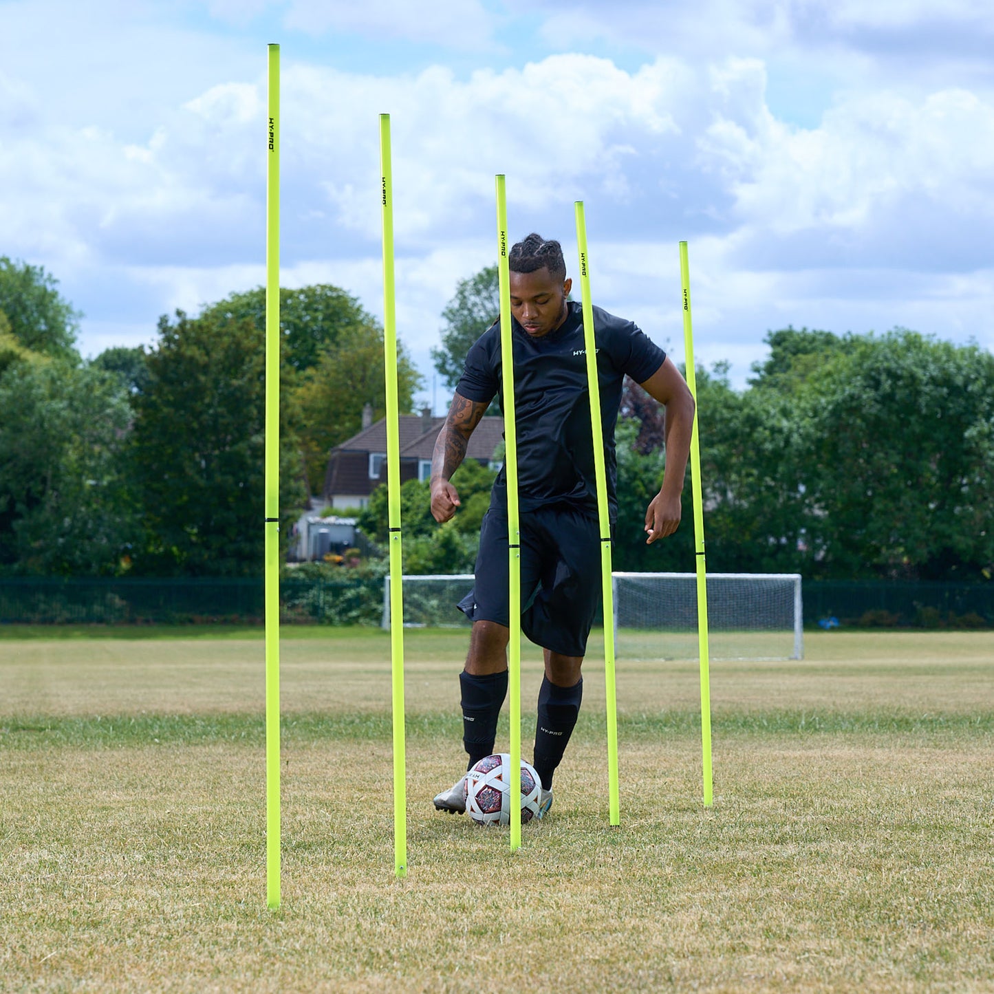 Hy-Pro Sports Yellow agility poles on a grass football field with a ball being dribbled through the poles by a football player