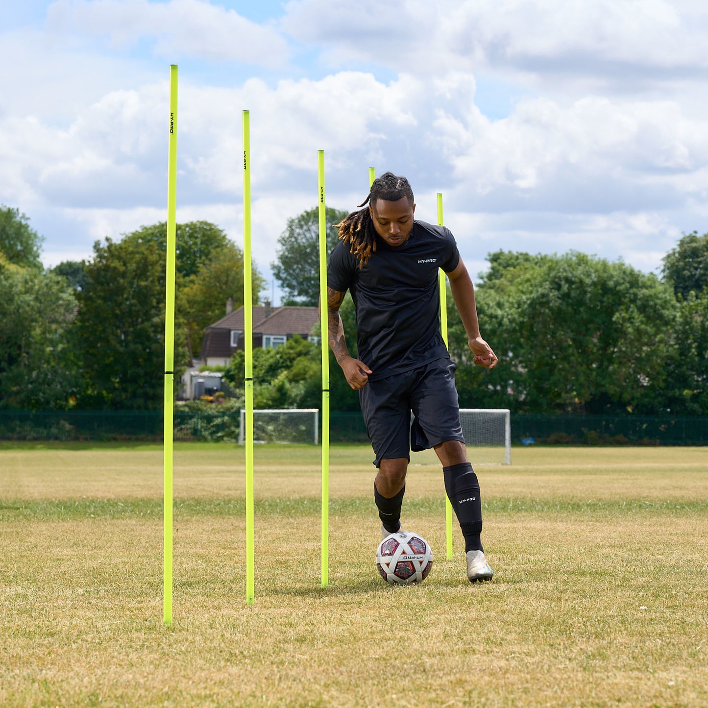 In action shot of a footballer quickly dribbling a ball around the Hy-Pro Sports agility poles on a grass field 