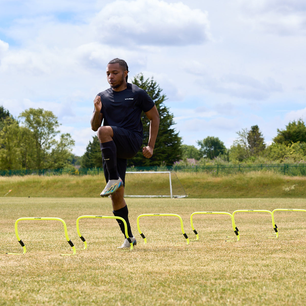 Man training agility on a grass football pitch using the adjustable Hy-Pro sports agility hurdles 