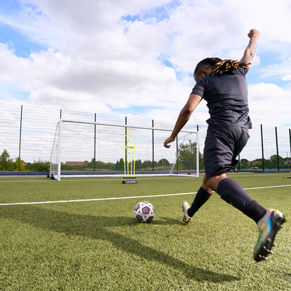 Adult Hy-Pro Defender Dummy with rubber base on an Astroturf pitch in front of a goal as a footballer kicks a ball towards the goal