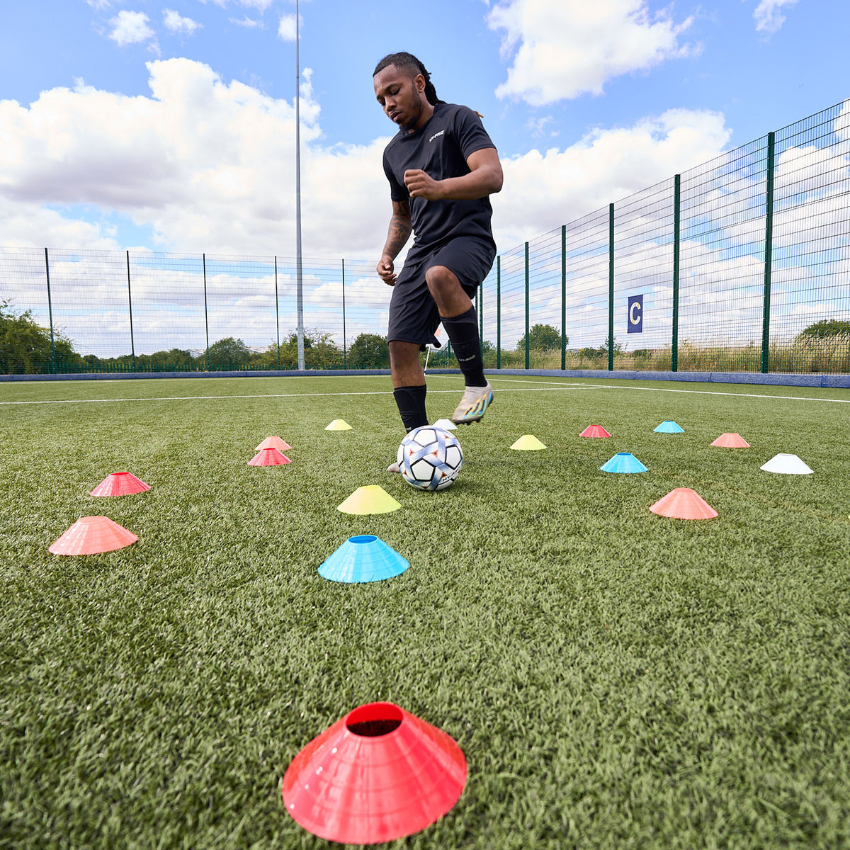 Footballer training dribbling skills on an Astroturf pitch using the scatter cone method with Hy-Pro Sports cones