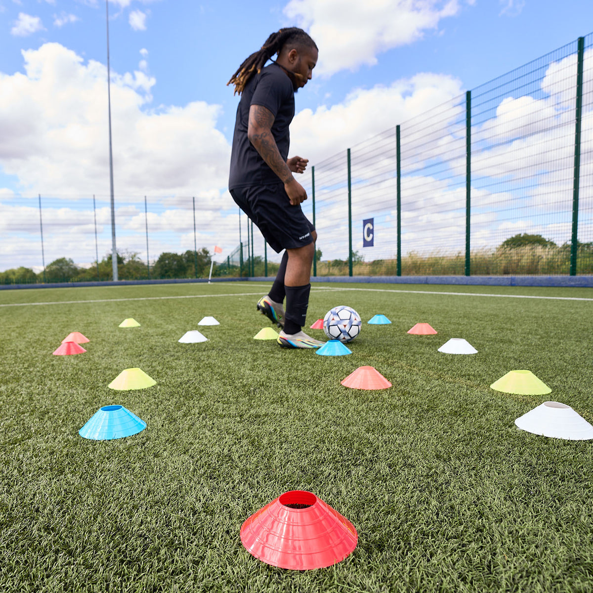 Football player dribbling football through scattered sports cones by Hy-Pro Sports on an Astroturf pitch