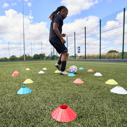 Football player dribbling football through scattered sports cones by Hy-Pro Sports on an Astroturf pitch