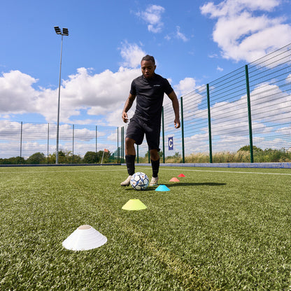 Football player dribbling FIFA training ball through Hy-Pro sports training cones on a pitch