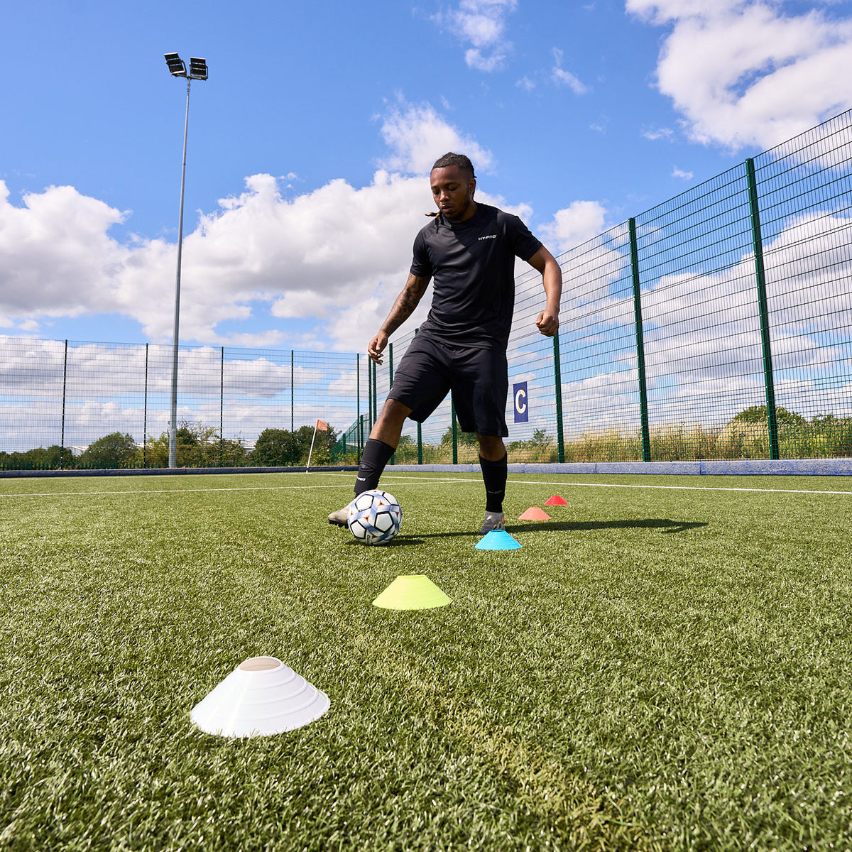 Footballer dribbling a ball through colourful Hy-Pro Sports training cones on a football pitch