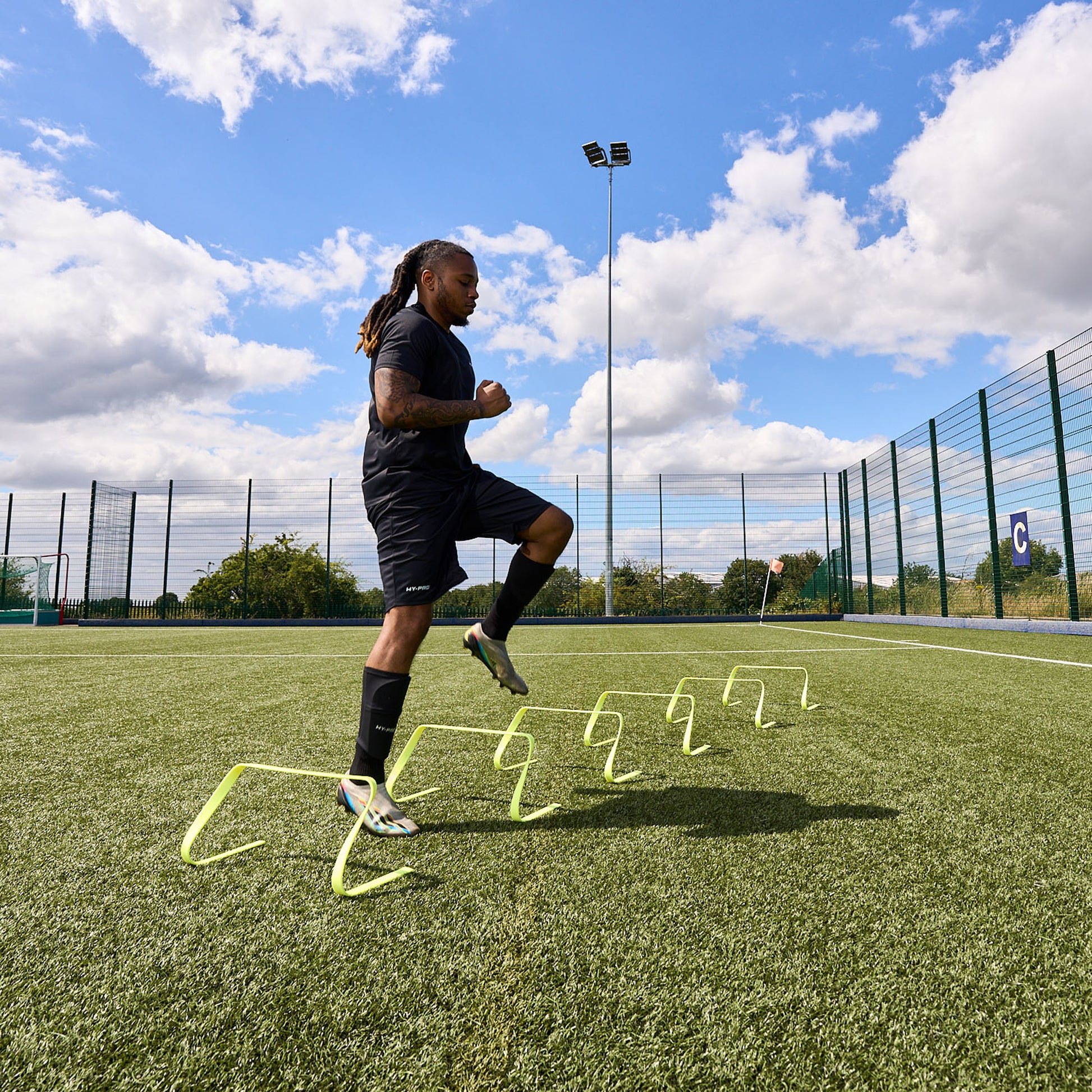 Football player training on an Astroturf pitch using the Hy-Pro sports flat agility hurdles. Doing sideways steps over each hurdle