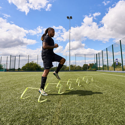 Football player training on an Astroturf pitch using the Hy-Pro sports flat agility hurdles. Doing sideways steps over each hurdle