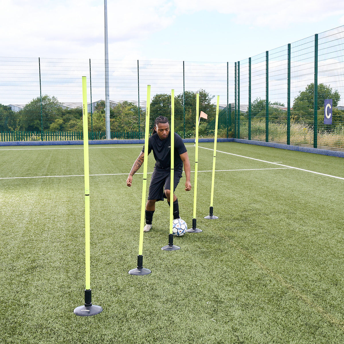 Agility poles and bases on a grass field with a footballer dribbling a ball through them
