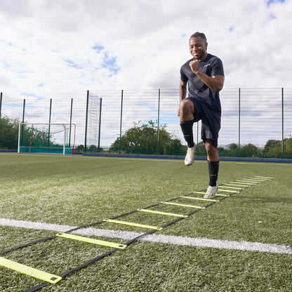 Smiling footballer uses the Hy-Pro Sports yellow agility ladder on an Astroturf football pitch to train agility 