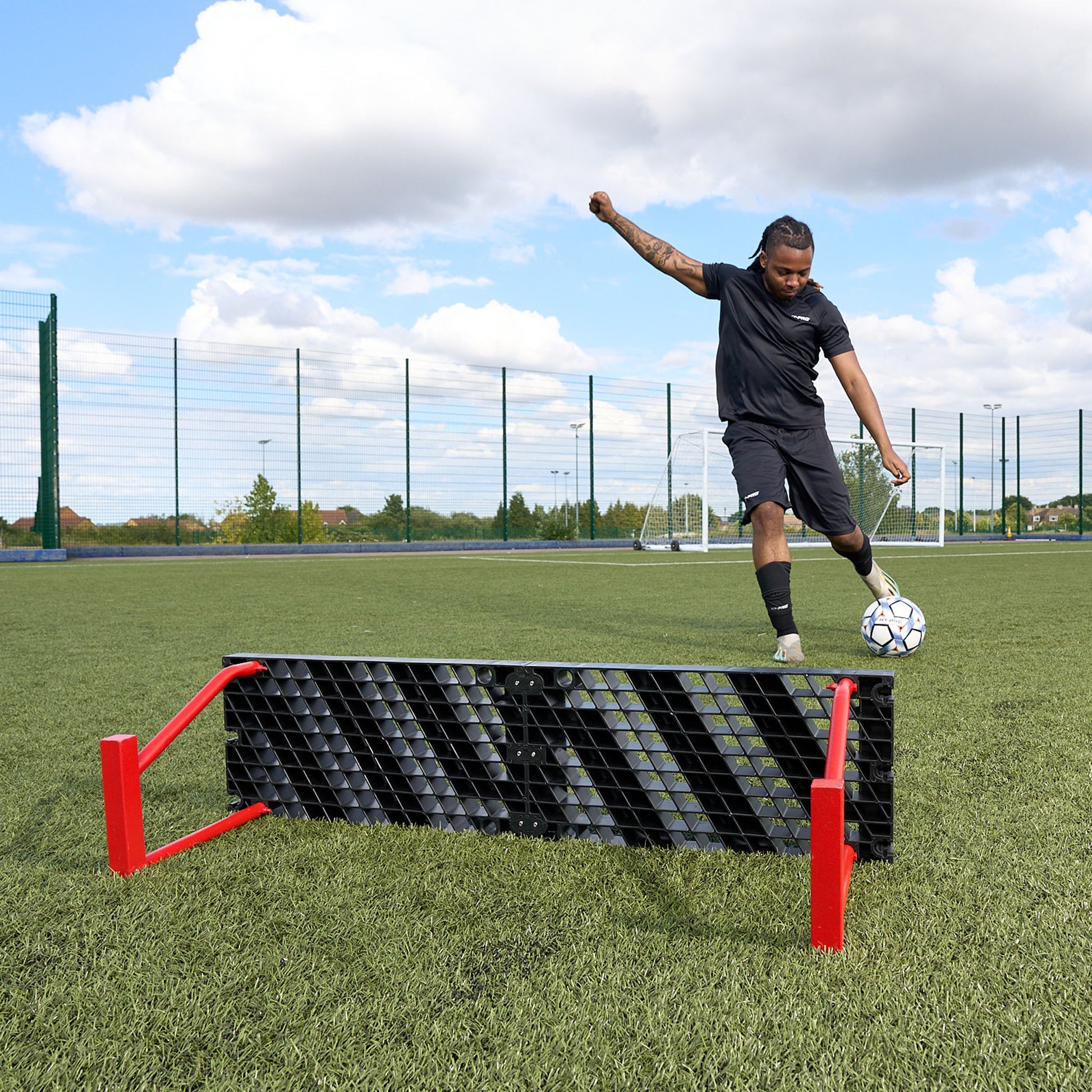 Photo from behind the Hy-Pro sports red and black football rebounder as a player kicks a ball towards the rebounder on a football pitch
