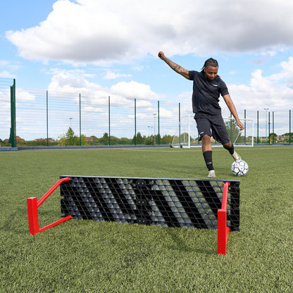 Photo from behind the Hy-Pro sports red and black football rebounder as a player kicks a ball towards the rebounder on a football pitch