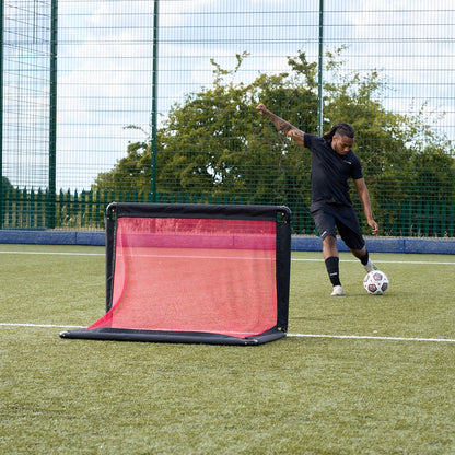 Photo from behind the football goal showing a footballer striking a football towards the hy-pro sports alu foldable goal in red and black on a grass pitch 