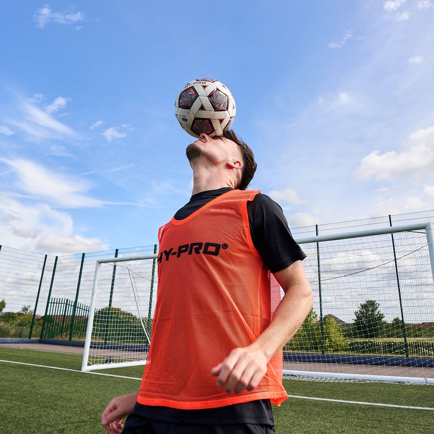 Football player balancing a ball on their head whilst wearing a bright Orange Hy-Pro sports bib