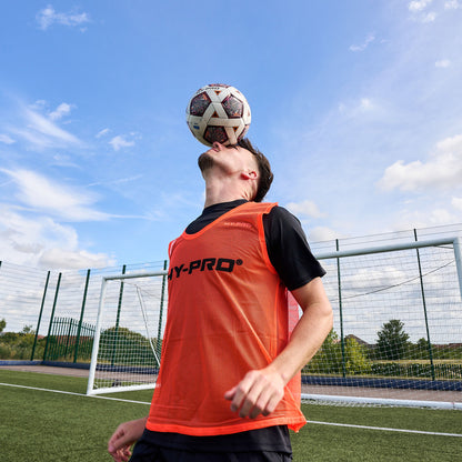 Football player balancing a ball on their head whilst wearing a bright Orange Hy-Pro sports bib