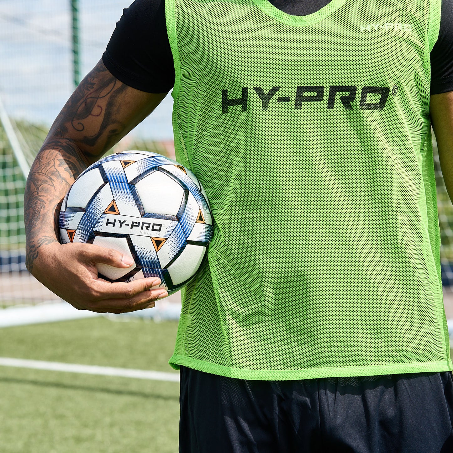 Hy-Pro Sports bib in Green with HY-PRO branding being worn by a football player on a pitch holding a football