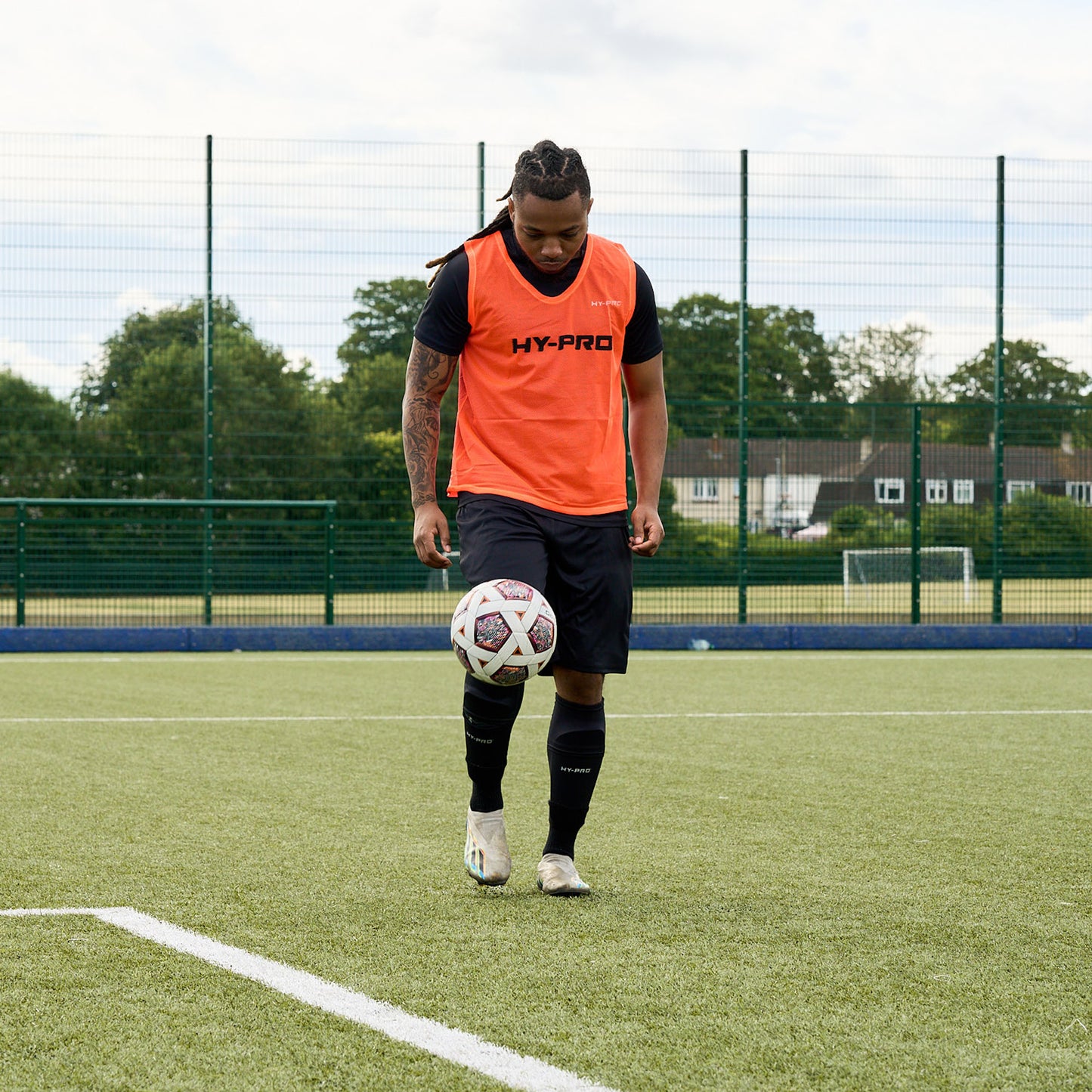 Hy-Pro Sports bib in Bright Orange being worn by a football player kicking the ball up in the air