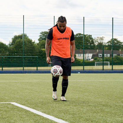 Hy-Pro Sports bib in Bright Orange being worn by a football player kicking the ball up in the air