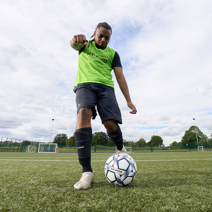 Hy-Pro sports bib in bright green being worn by a football player kicking a ball across a pitch