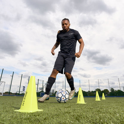 Footballer dribbling a ball through Hy-Pro yellow sports cones on a grass pitch