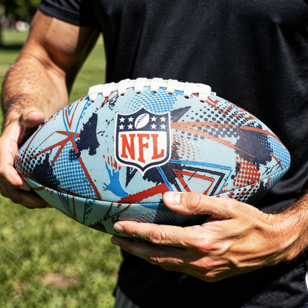 NFL Neoprene football in blue and red with NFL logo being held by someone on the grass