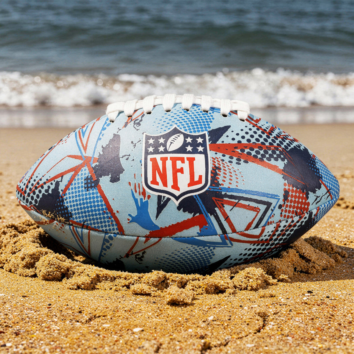 NFL Neoprene football in blue and red with NFL logo on a sandy beach with sea in the background