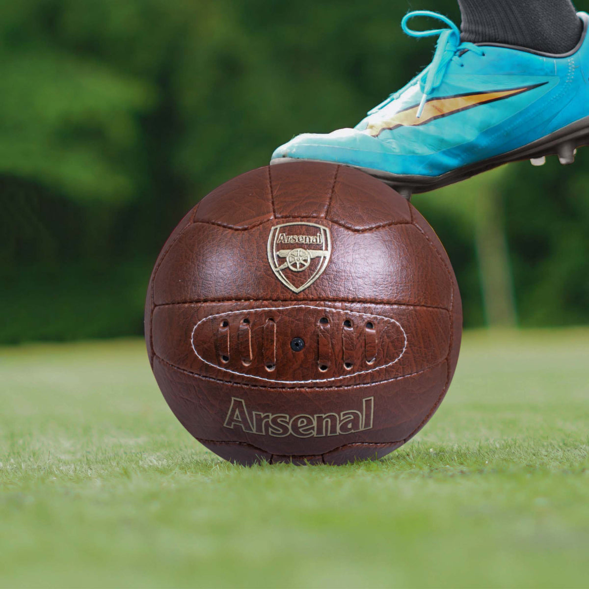 Arsenal Faux Leather Retro Football being held in place on a grass field by a football boot